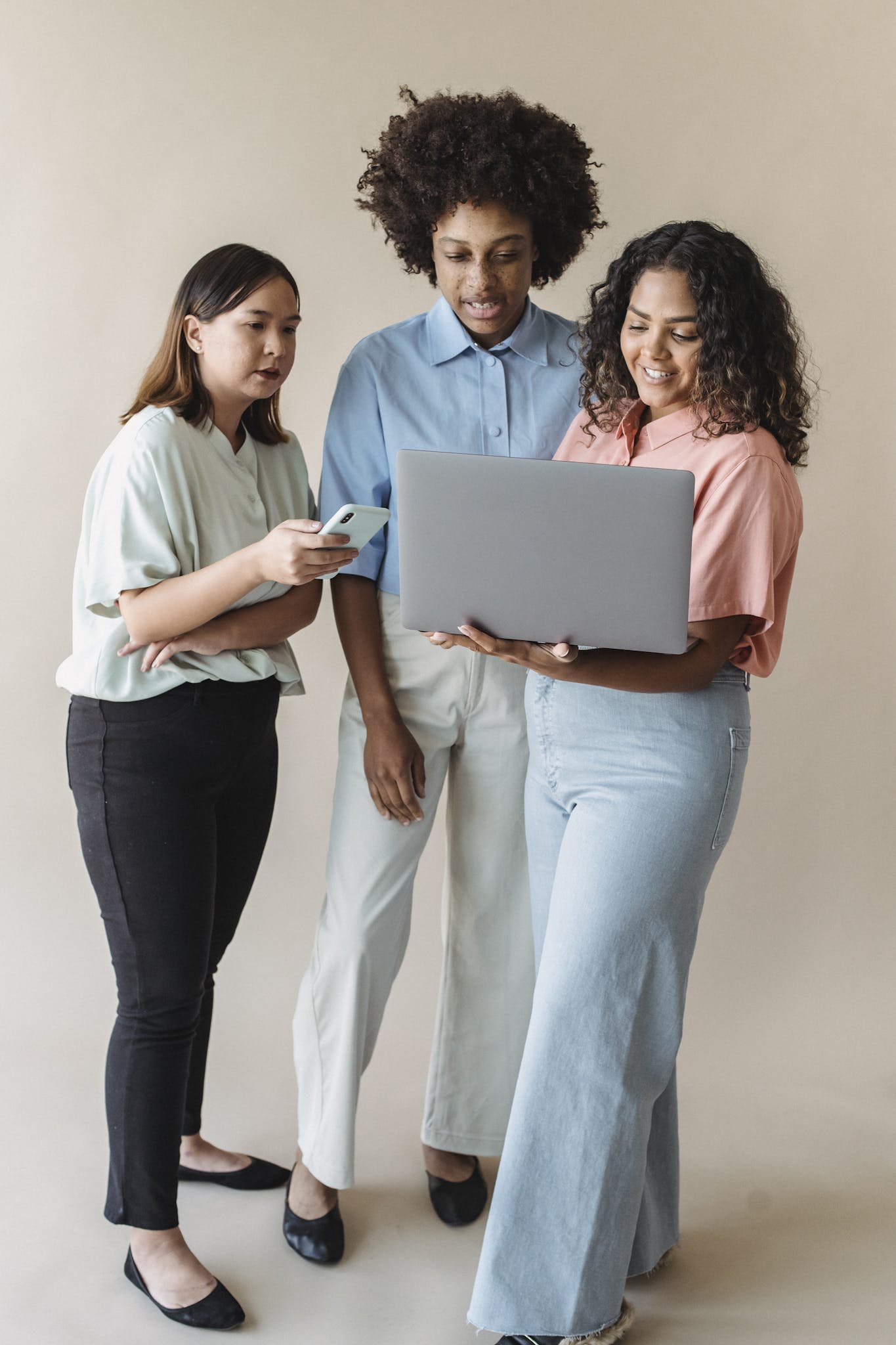 Three diverse women collaborating using a laptop and smartphone in a modern setting.